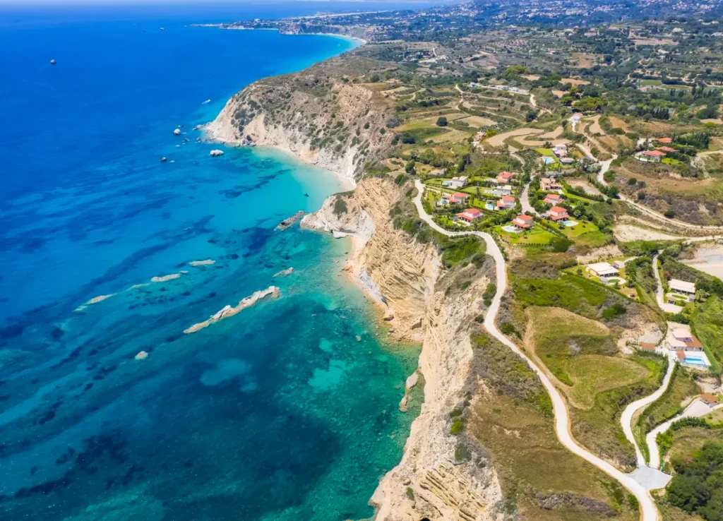 Aerial view of cliffside houses with winding roads and turquoise waters along a scenic coastal landscape