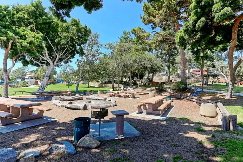 Public park with picnic tables, barbecue grill, shaded trees, and open grassy area for gatherings