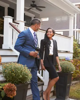 Real estate agent and client smiling while touring a residential home, standing by the front porch with potted flowers