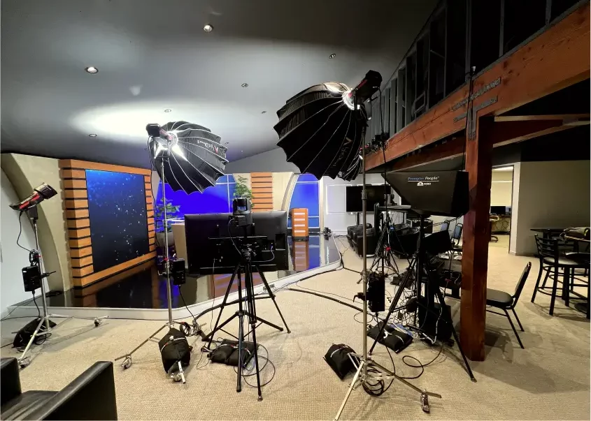 Professional video studio with lighting umbrellas, cameras, monitors, and broadcast set background